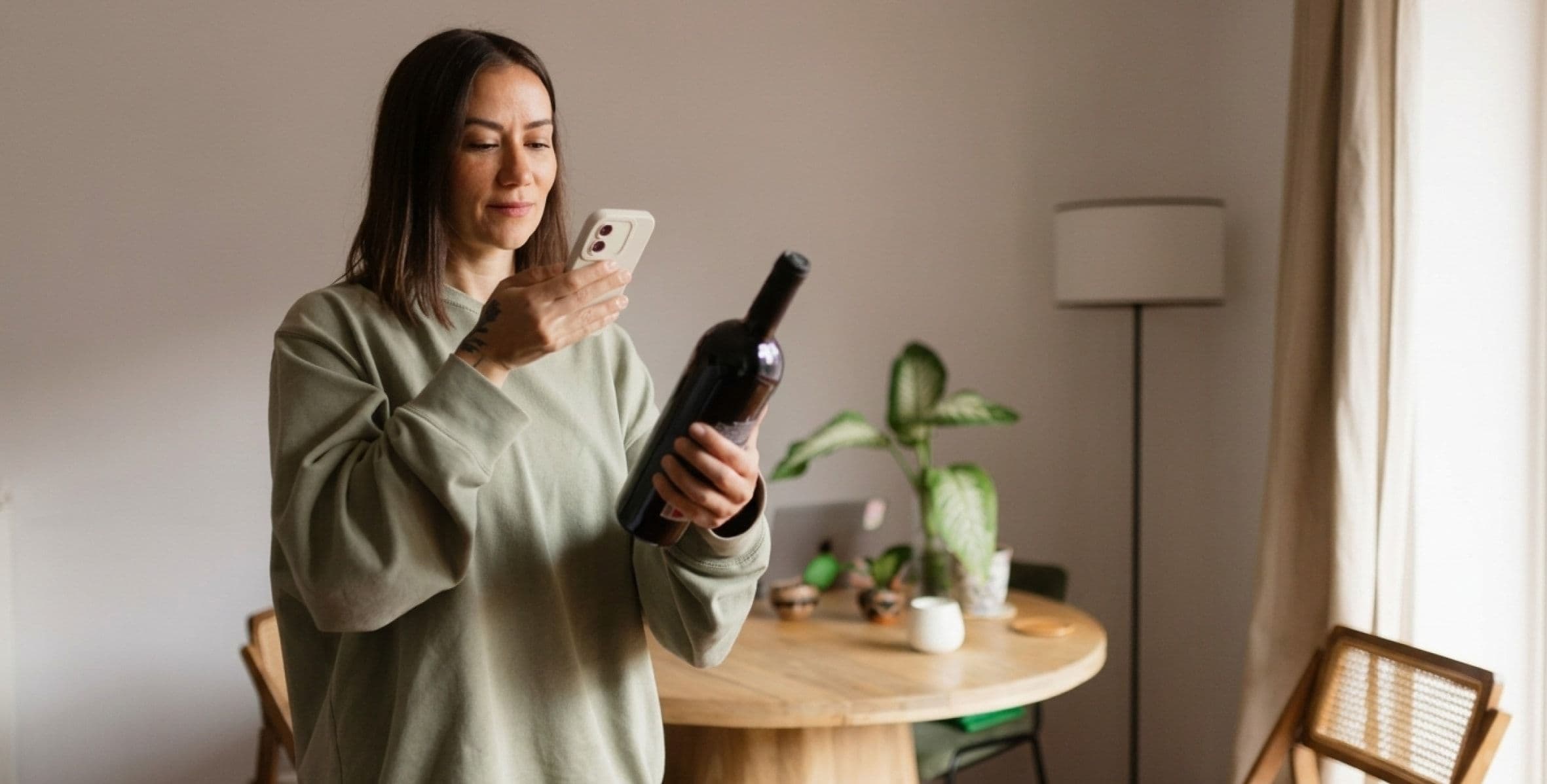 A woman at home photographing a bottle of wine with her phone