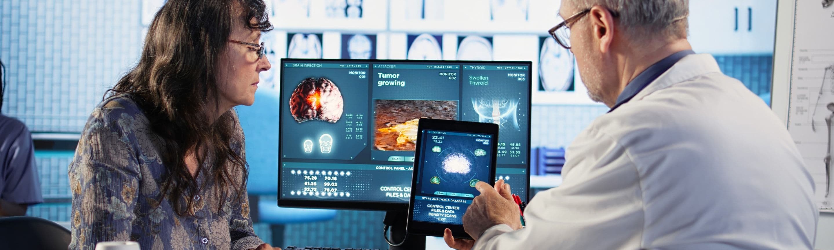 A doctor and a colleague reviewing scans on a monitor and a tablet