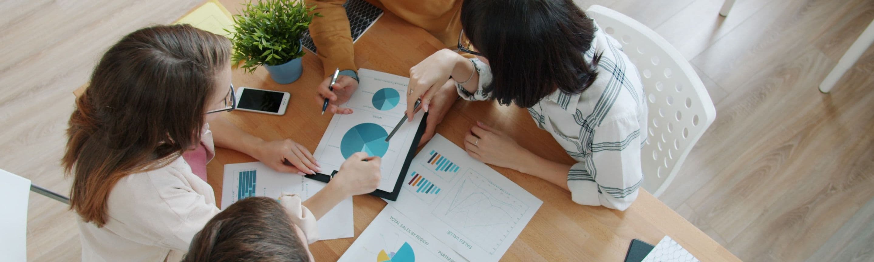 A team leaning over charts and a laptop on a table, seen from above