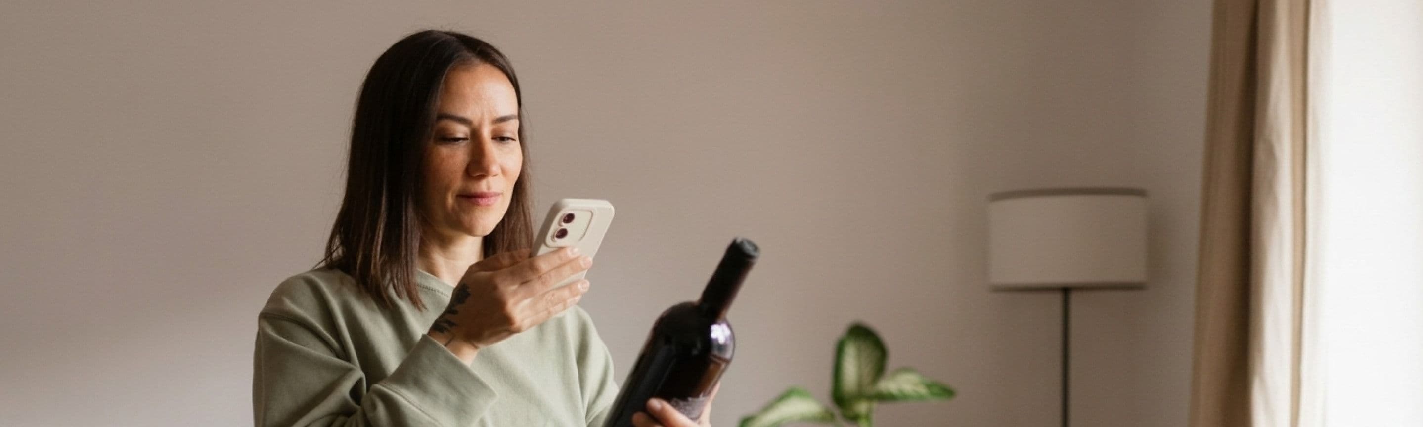 A woman at home photographing a bottle of wine with her phone