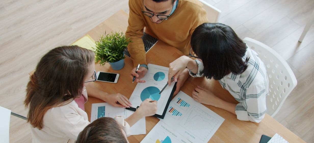 A team leaning over charts and a laptop on a table, seen from above