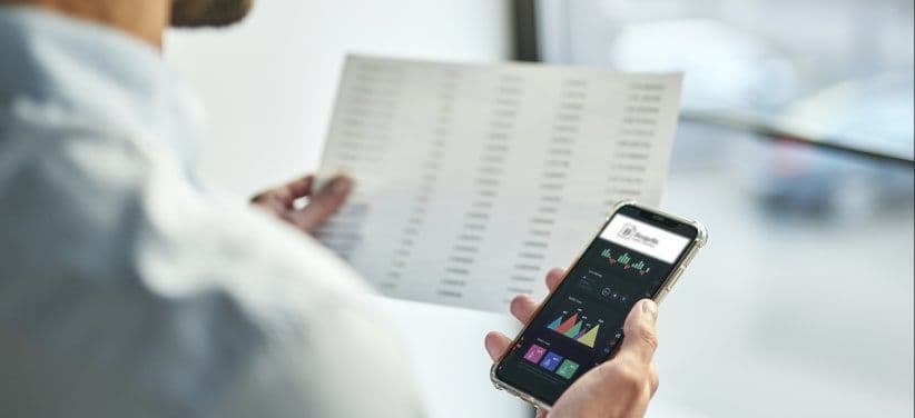 A hand holding a phone open on the Borgella app beside a printed report