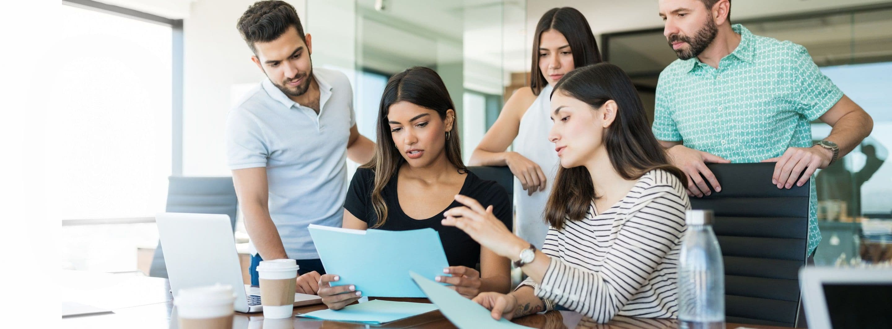 Five colleagues gathered around a table, reviewing papers together in a bright office