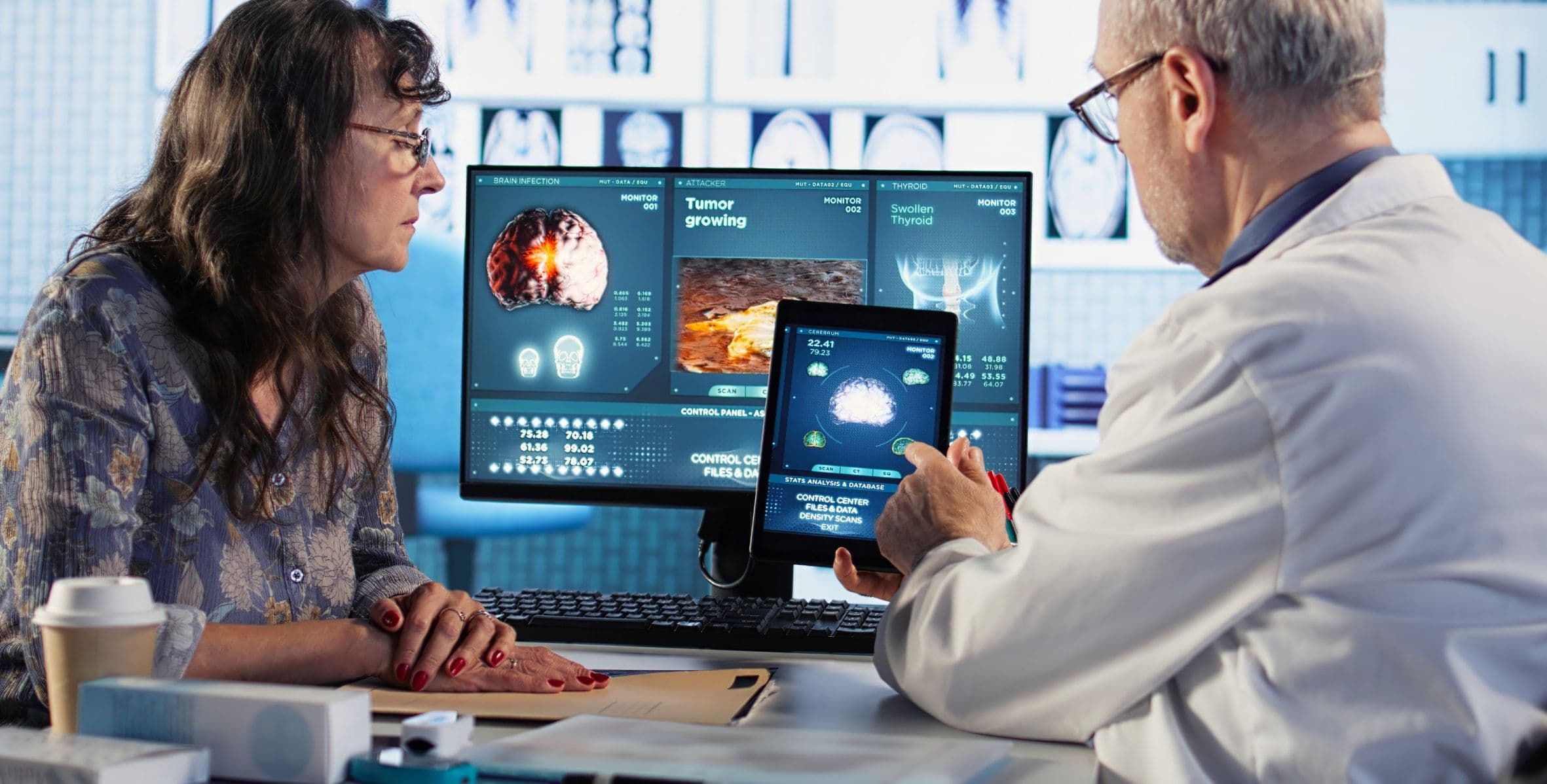 A doctor and a colleague reviewing scans on a monitor and a tablet